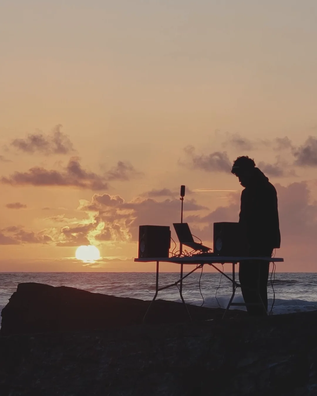 DJ set Horison au coucher du soleil, un DJ en silhouette derrière ses platines face à la mer
