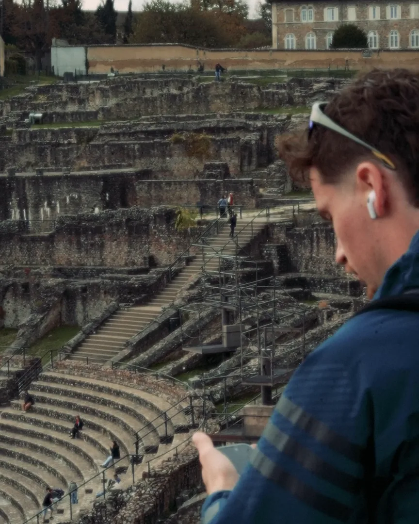Écouteur à l’oreille, un auditeur suit un guide audio Horison face au théâtre antique de Fourvière