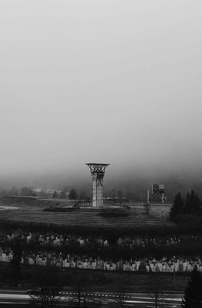 Une tour en béton dans la brume au-dessus d’une vallée, en noir et blanc